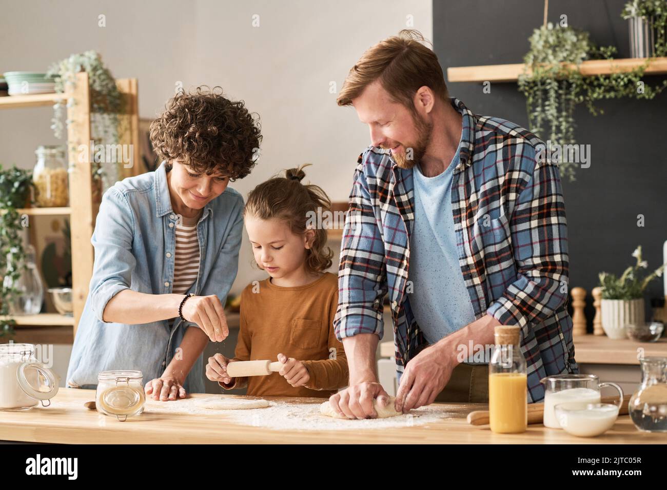 Parents teaching their little son to bake homemade pie from dough at table in kitchen Stock Photo
