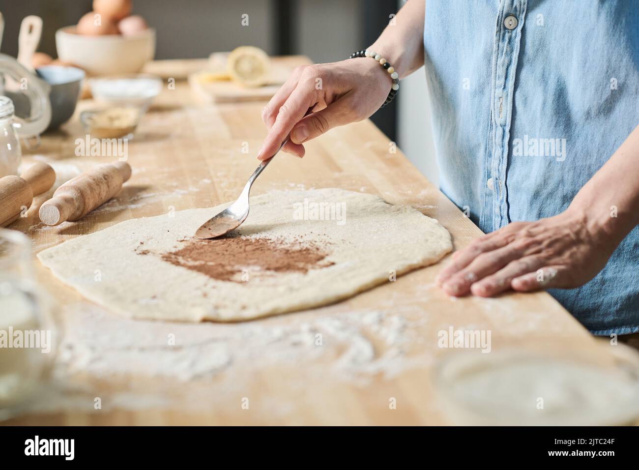 Close-up of housewife adding cinnamon with spoon to dough to bake buns in kitchen Stock Photo