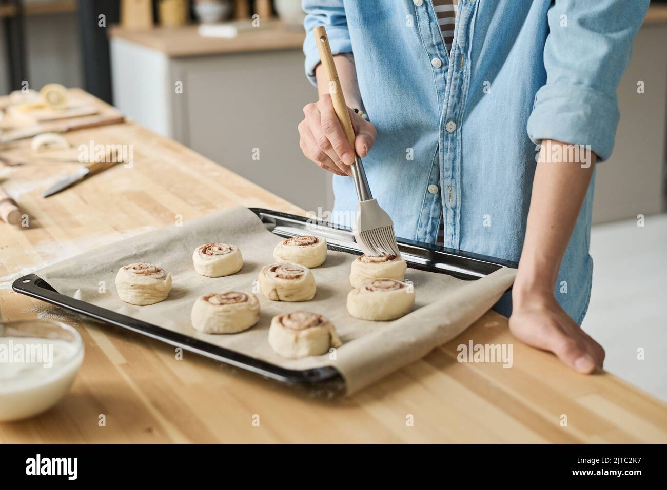 Close-up of young woman using brush to oil buns on tray before baking Stock Photo