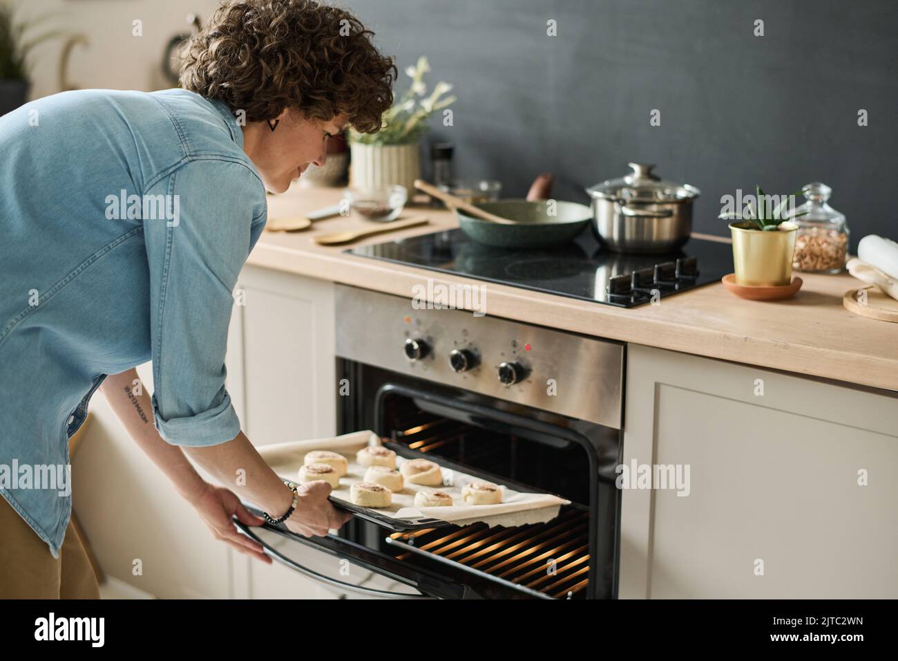 Young woman putting tray with sugar buns in the oven in domestic kitchen Stock Photo
