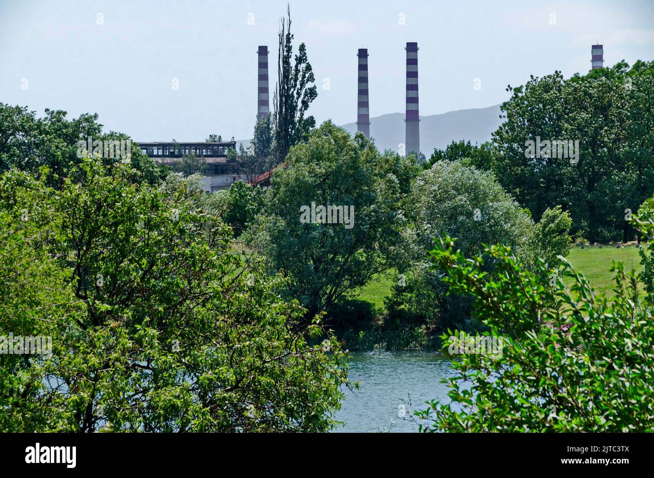 Spring green fresh trees and lake in residential area Drujba against the background of the chimneys of the Thermal Power Plant, Sofia, Bulgaria Stock Photo