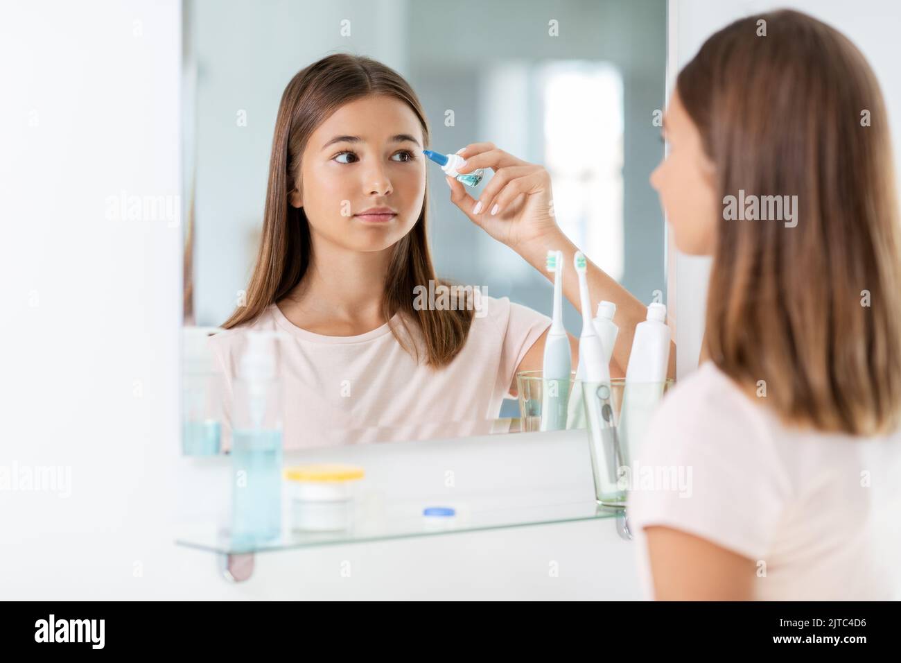 teenage girl with eye drops in front of mirror Stock Photo