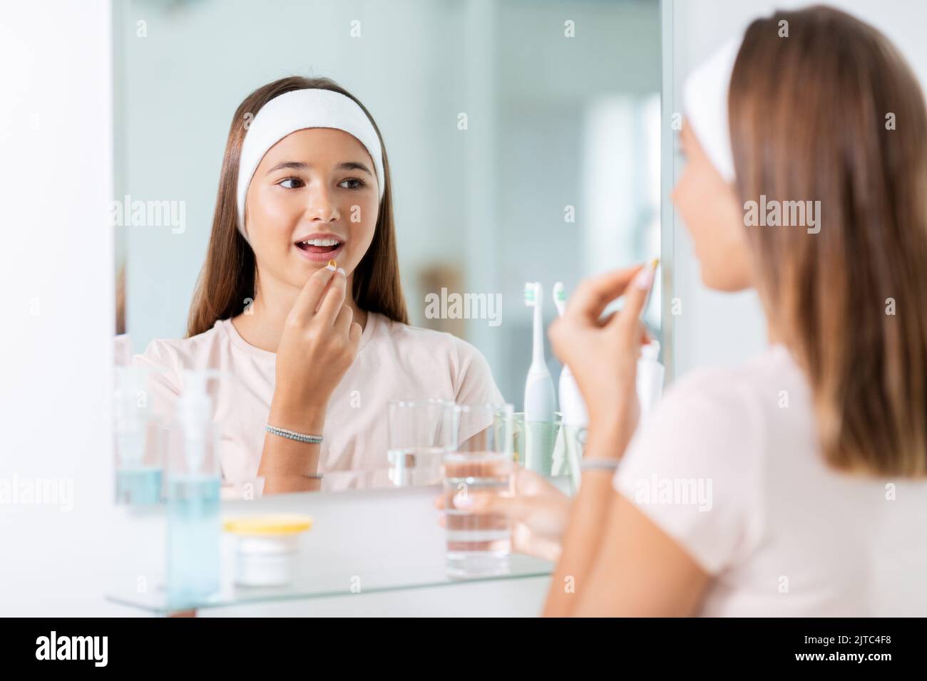 teenage girl taking cod liver oil at mirror Stock Photo