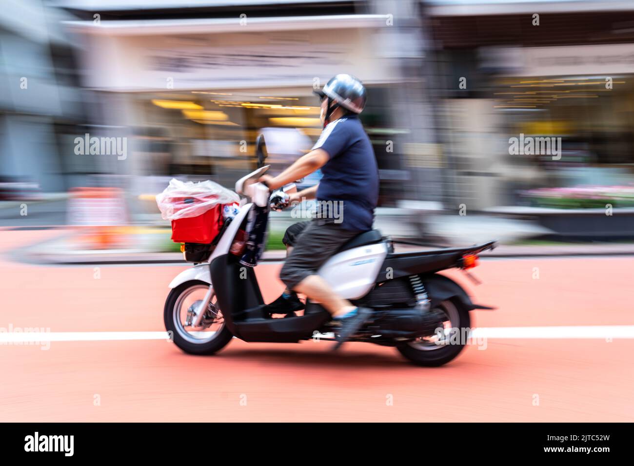 A electric delivery scooter rushes down Orange Street near the Sensoji temple in Asakusa, Tokyo, Japan. Stock Photo