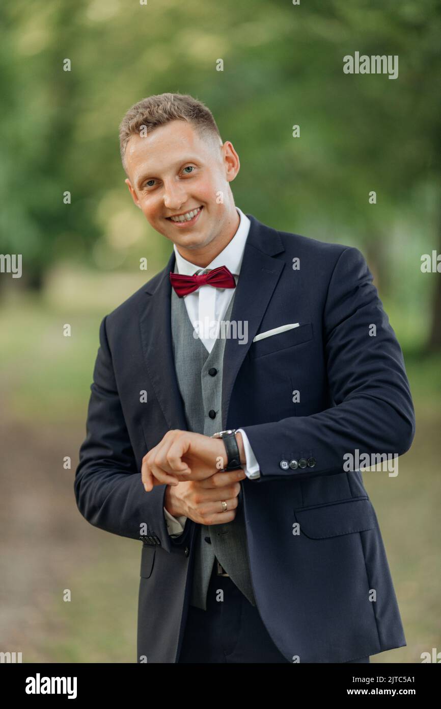 Vertical portrait of confident, handsome smiling blond businessman or groom in formal tuxedo fixing stylish hand watch Stock Photo