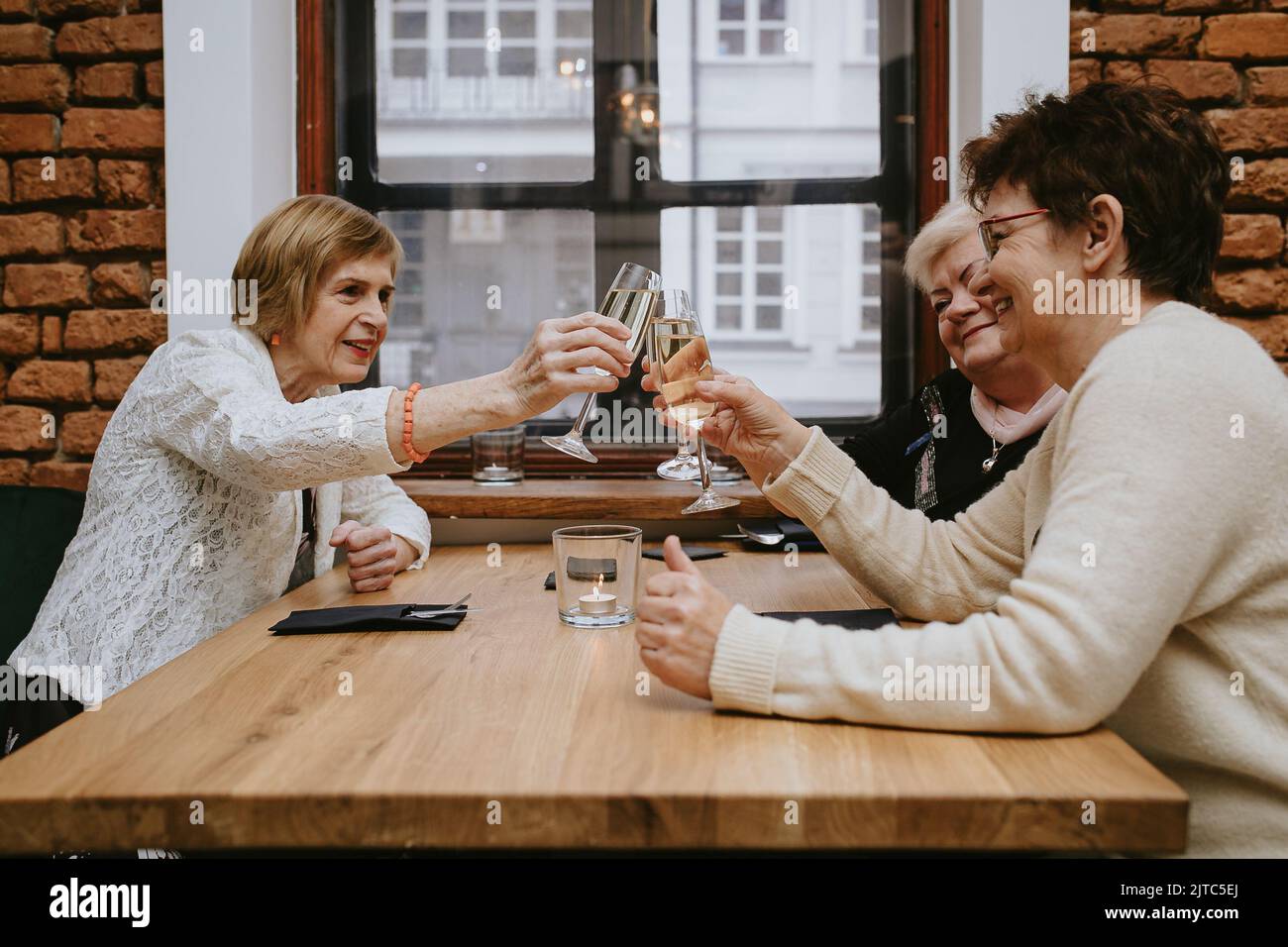 Three senior women friends having dinner at restaurant, attractive lady spending time together indoors. old friends drinking wine in modern apartment Stock Photo