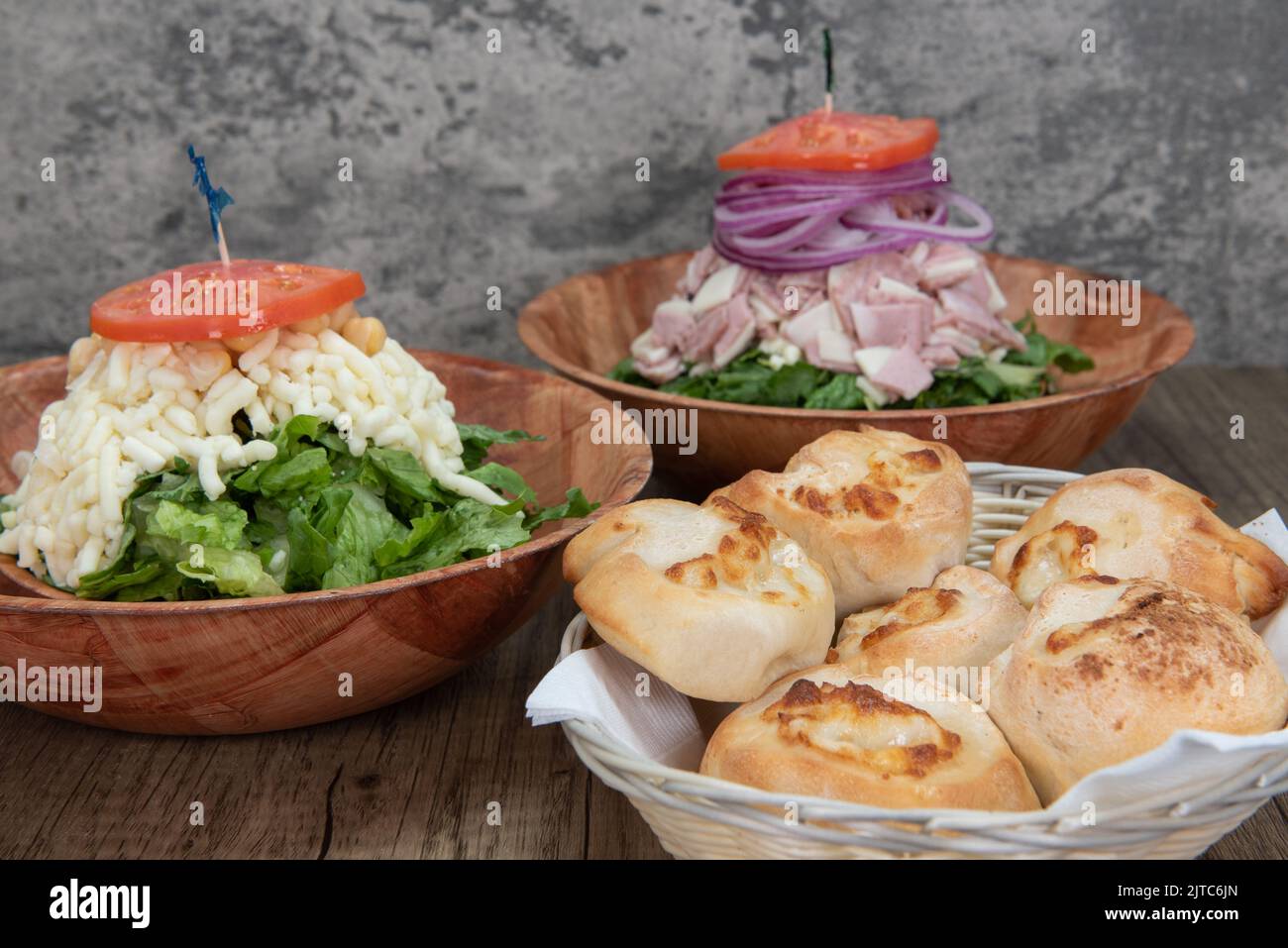 Italian food feast is set up on the table with two salads to choose from or a basket of garlic and cheese rolls. Stock Photo