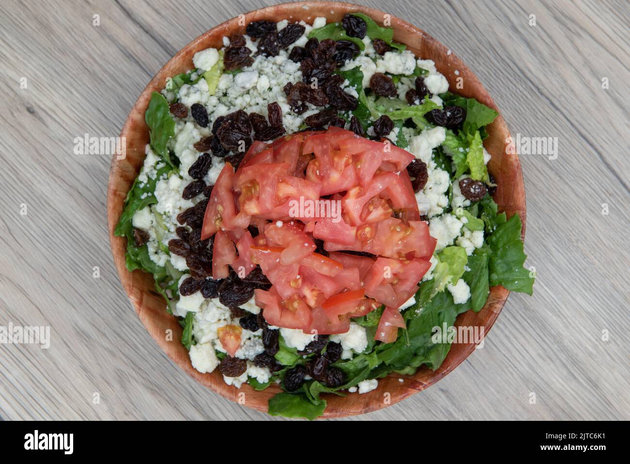 Overhead view of bleu cheese and walnut salad is delicately balanced tall with chopped tomato, raisins, and romaine lettuce and is a meal within itsel Stock Photo