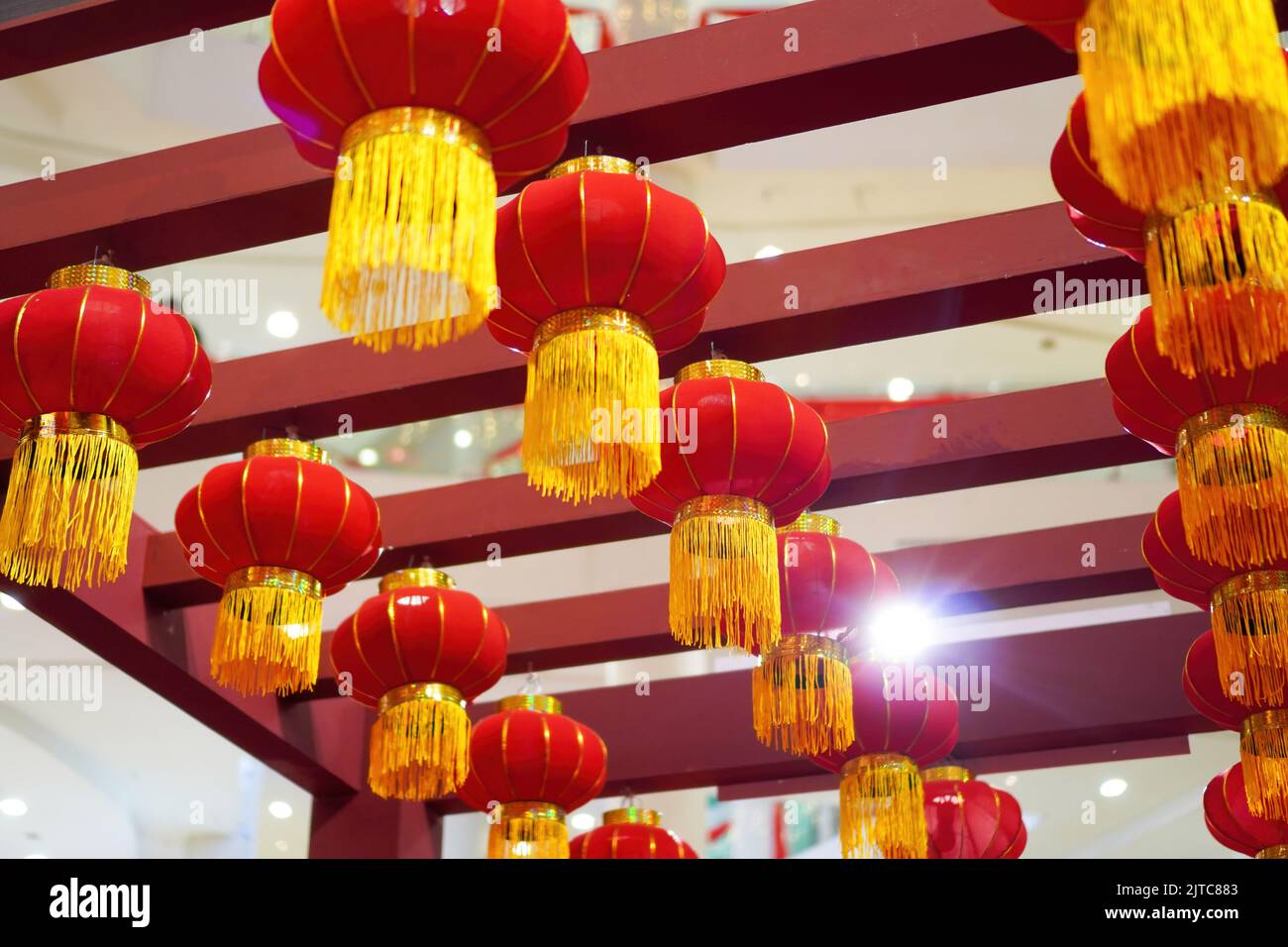 A low angle shot of a series of Chinese red lanterns with yellow strips, hanging from red pieces of wood for New Year decoration Stock Photo