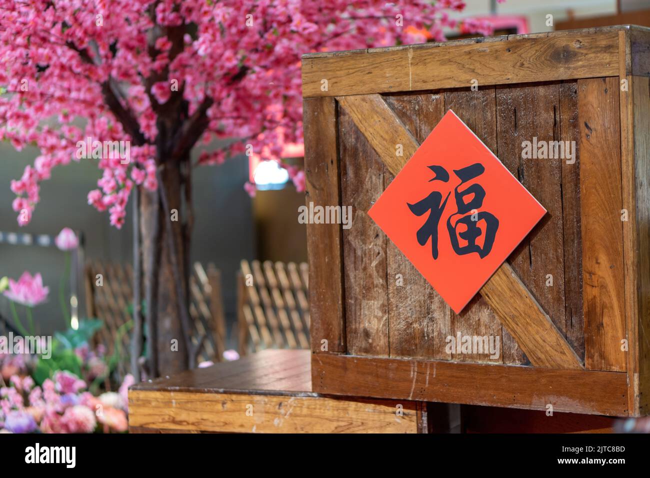 A closeup shot of Chinese calligraphy hung on a brown wooden box with a pink Cherry blossom tree in the background  Translation: good fortune, luck Stock Photo