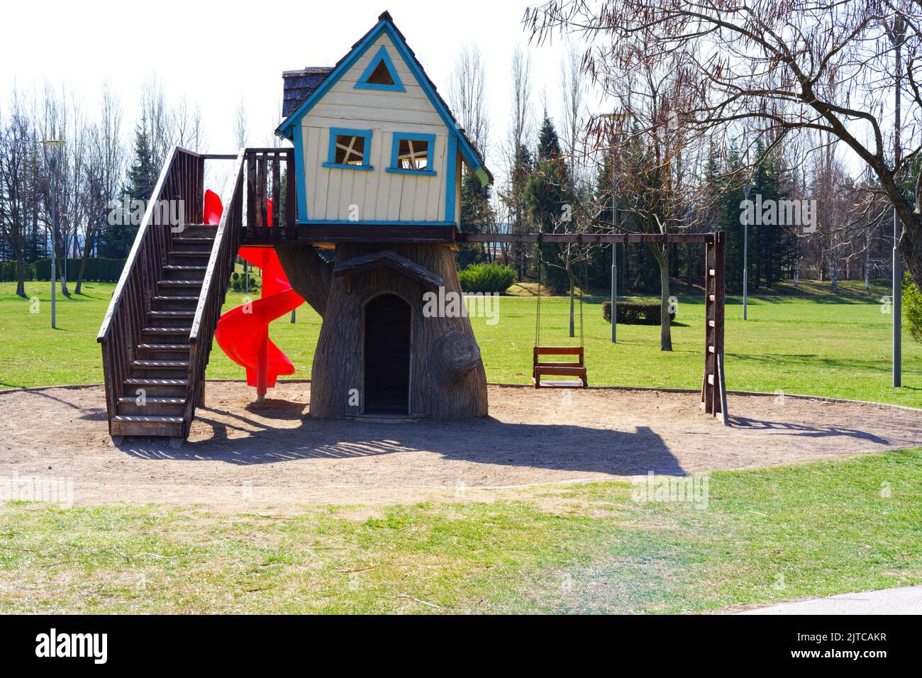 Wood house kids' playground with red slide and swings in a sunny day at