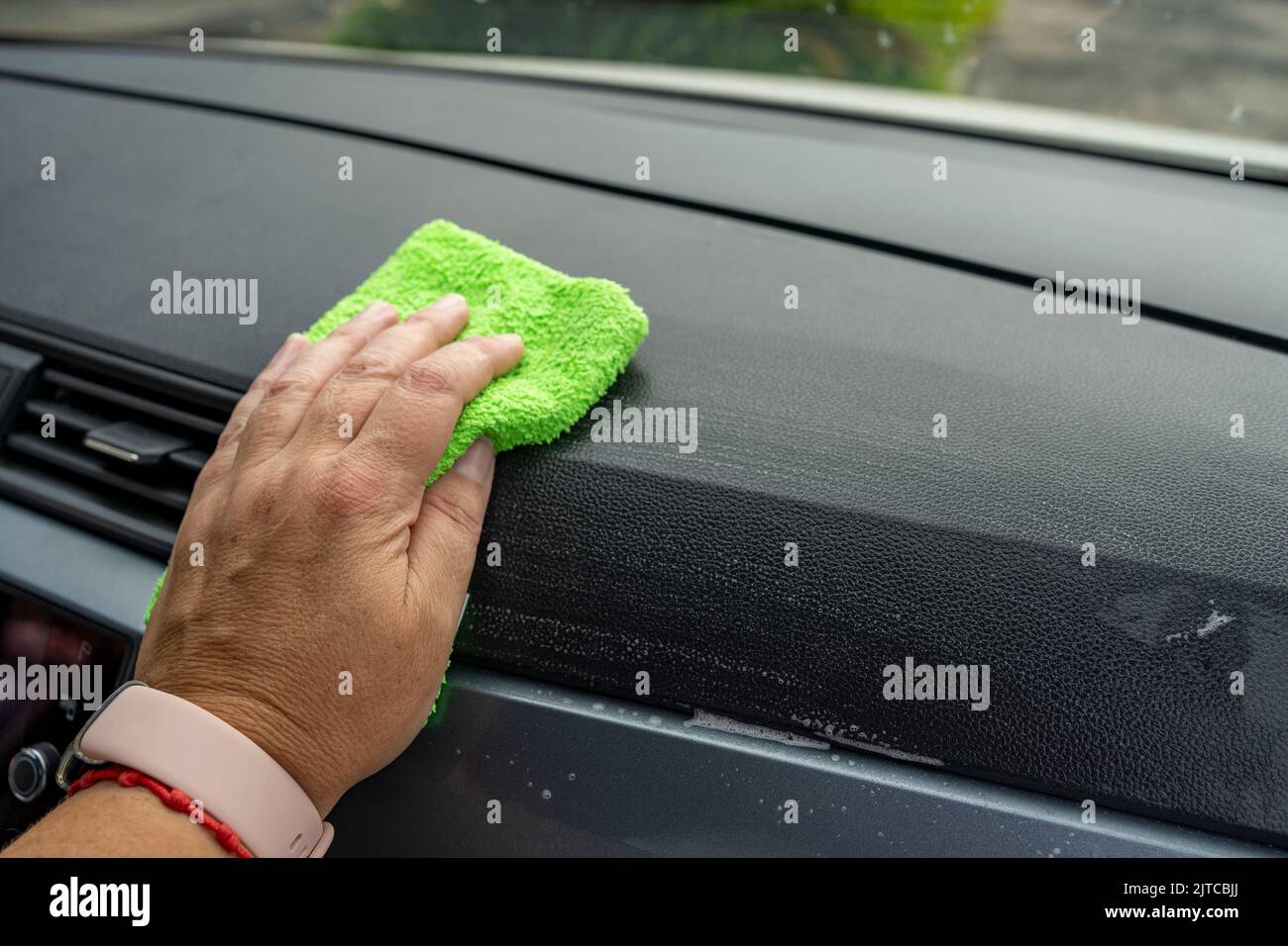 hand wiping the dashboard of a car with a green cloth Stock Photo