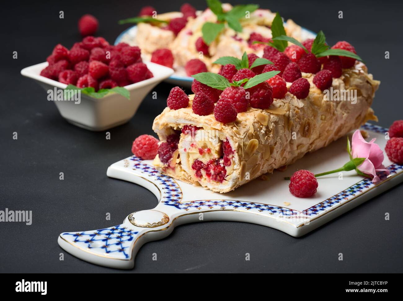 Baked meringue roll with cream and fresh red raspberry on a black
