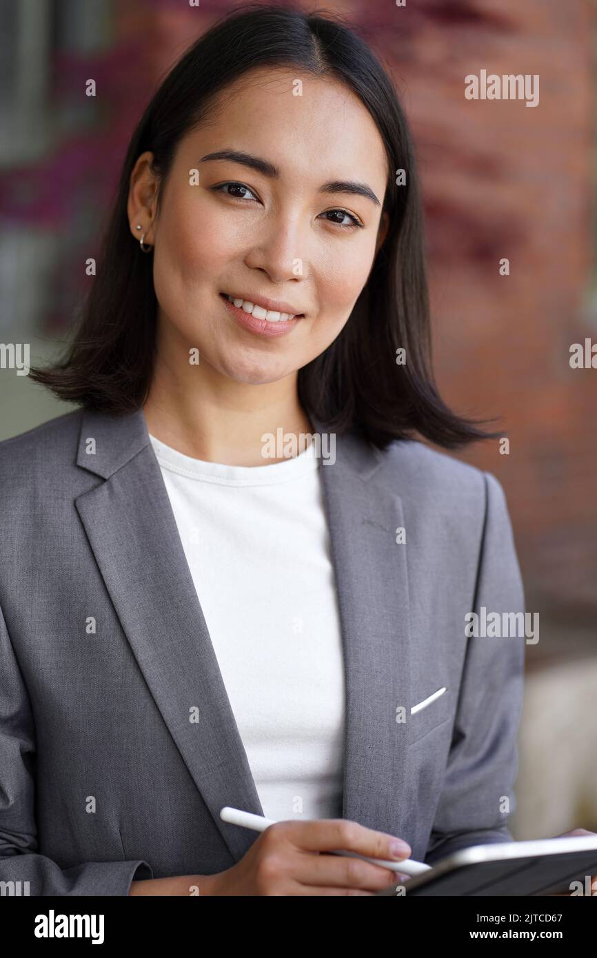 Smiling young Asian woman entrepreneur wearing suit, vertical headshot portrait. Stock Photo