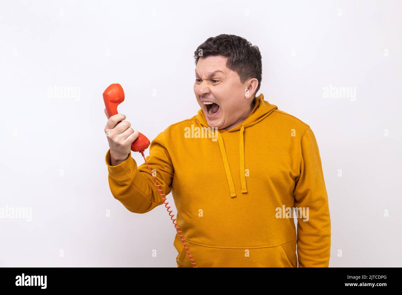 Portrait of nervous man screaming and yelling talking retro landline phone, complaining on connection quality, wearing urban style hoodie. Indoor studio shot isolated on white background. Stock Photo