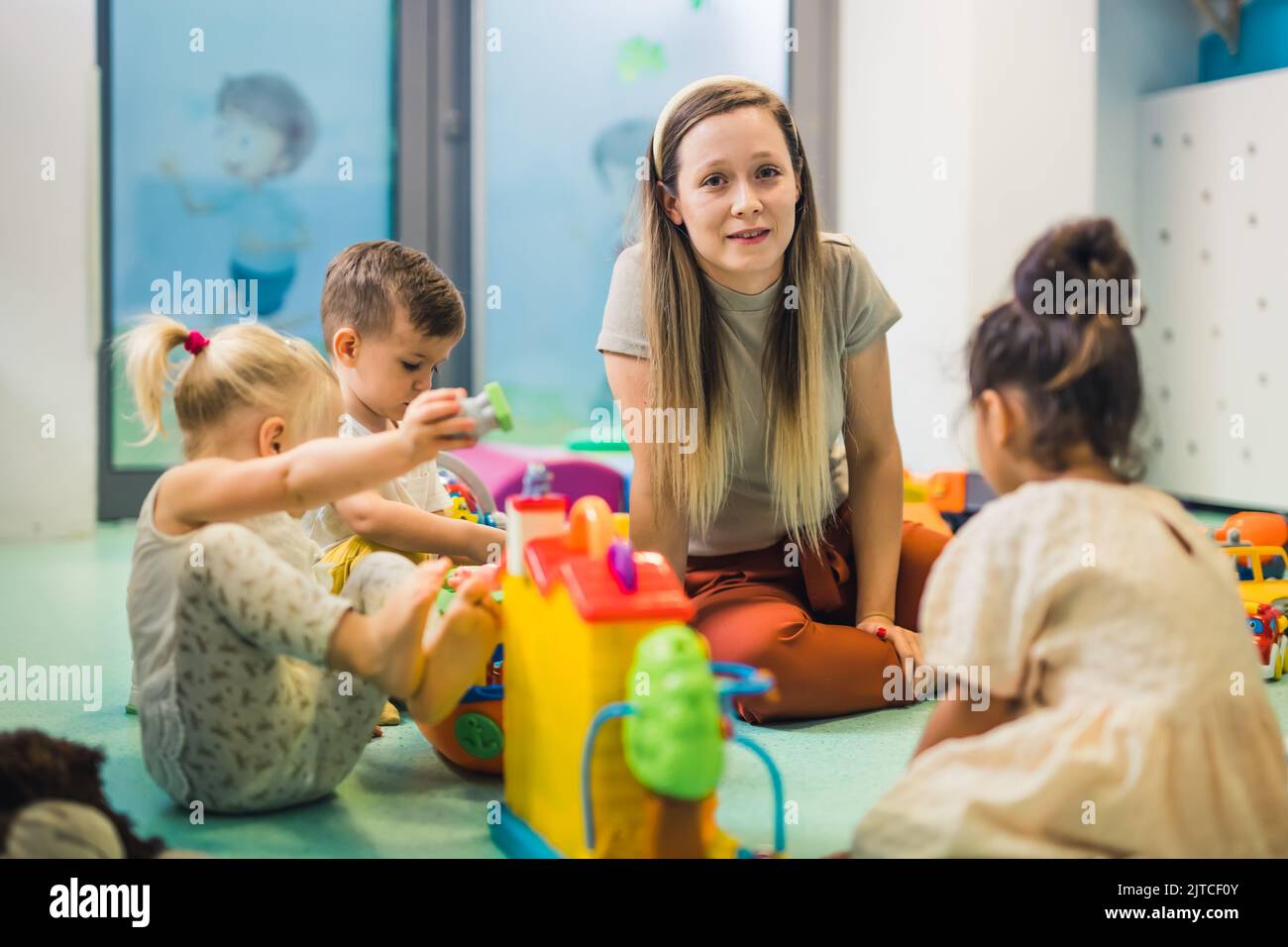 Nursery school. Toddlers and their teacher playing with colorful plastic playhouses, cars and boats. Imagination, creativity, fine motor and gross motor skills development. High quality photo Stock Photo