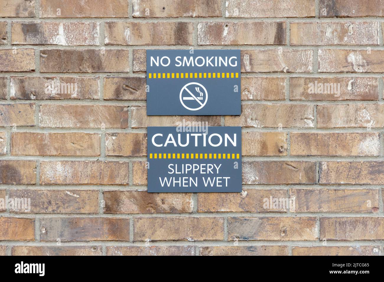 Warning signs No smoking and Slippery when wet on brick wall, warning labels on gray plates Stock Photo