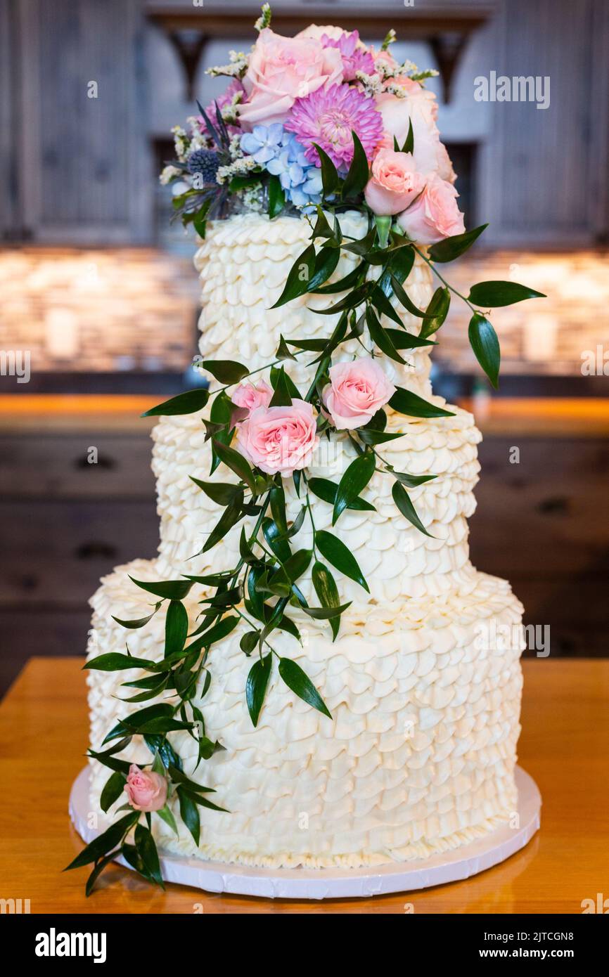 White wedding cake with cascading pink and purple flowers and leaves sitting on a counter. Stock Photo