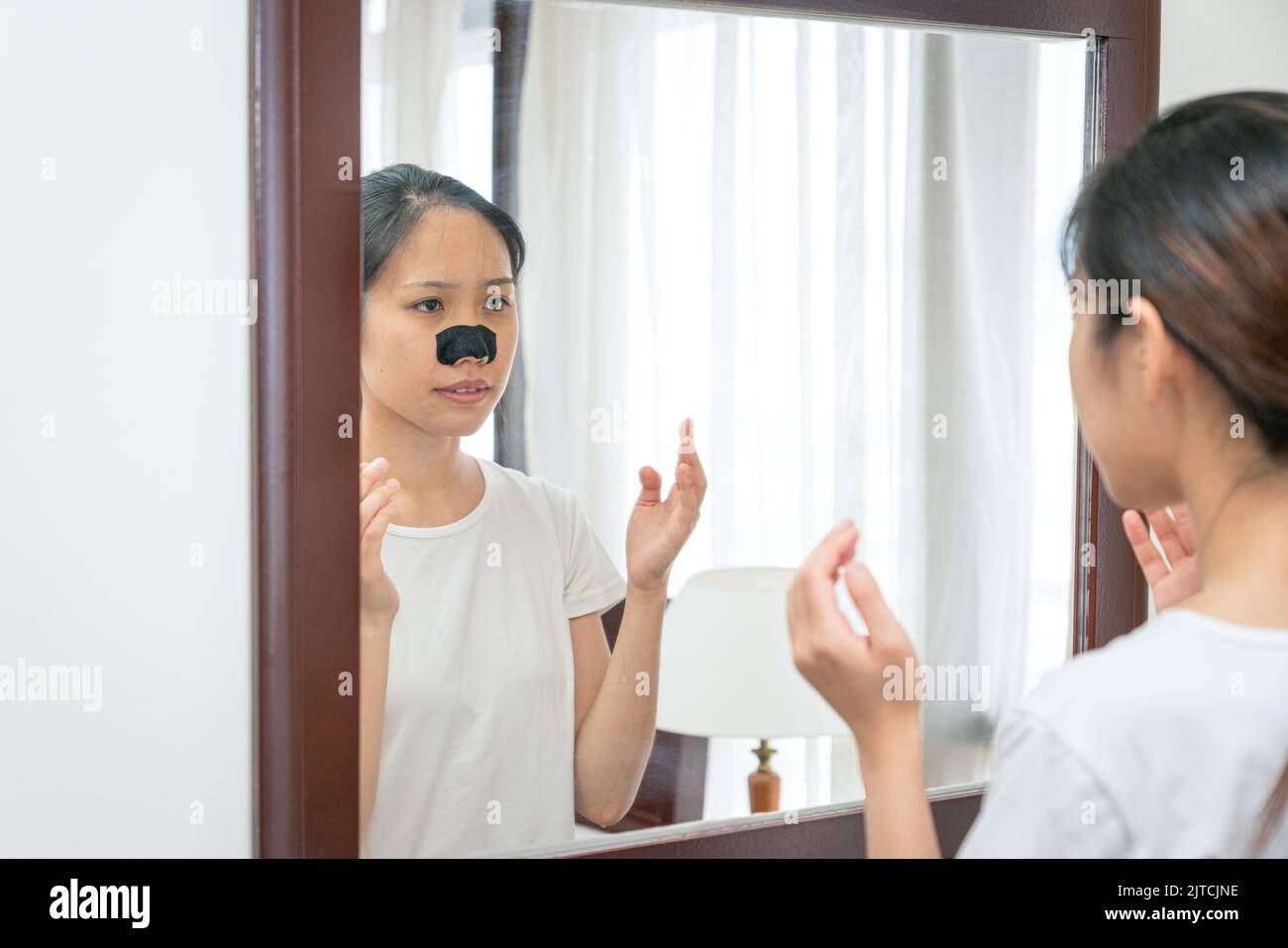 Beautiful Asian woman looking at the mirror, applying mask charcoal deep cleansing nose pore strip on fresh clean skin. Beauty and skin care treatment Stock Photo
