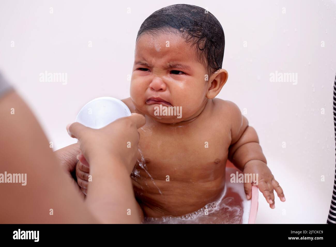 A baby crying during bath time that is upset due to water being sprayed by caregiver, to rinse the shampoo off her short hair. Stock Photo
