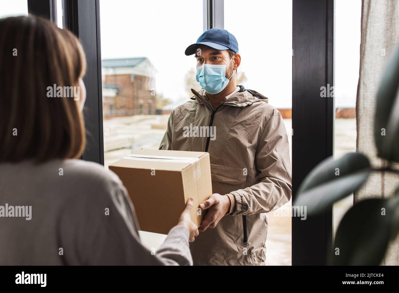 delivery man in mask giving parcel to customer Stock Photo - Alamy