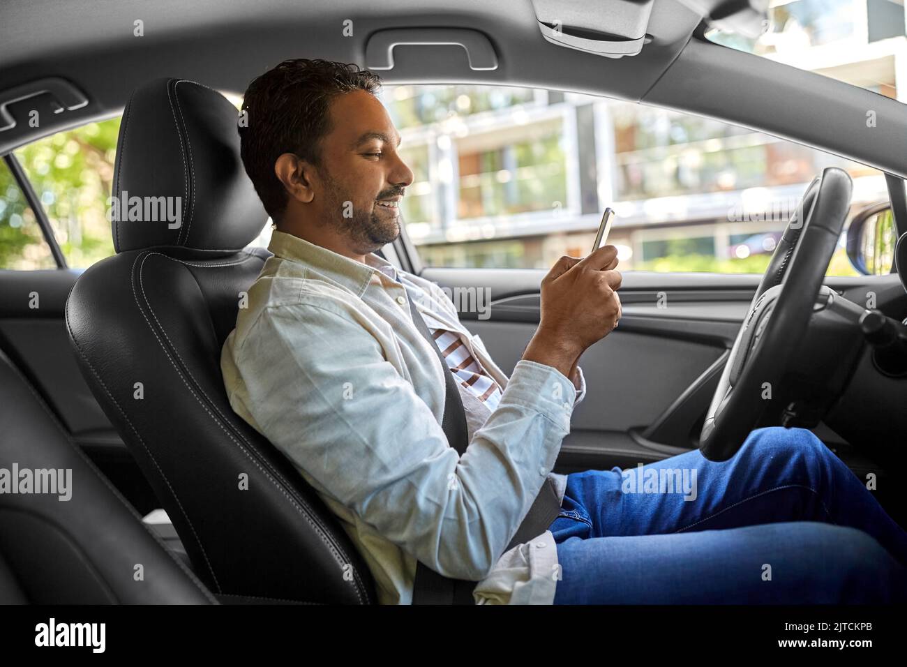 smiling indian man in car using smartphone Stock Photo