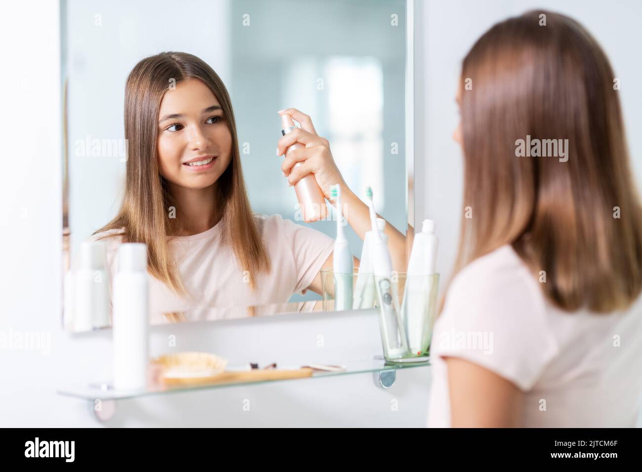 teenage girl using hair styling spray at bathroom Stock Photo