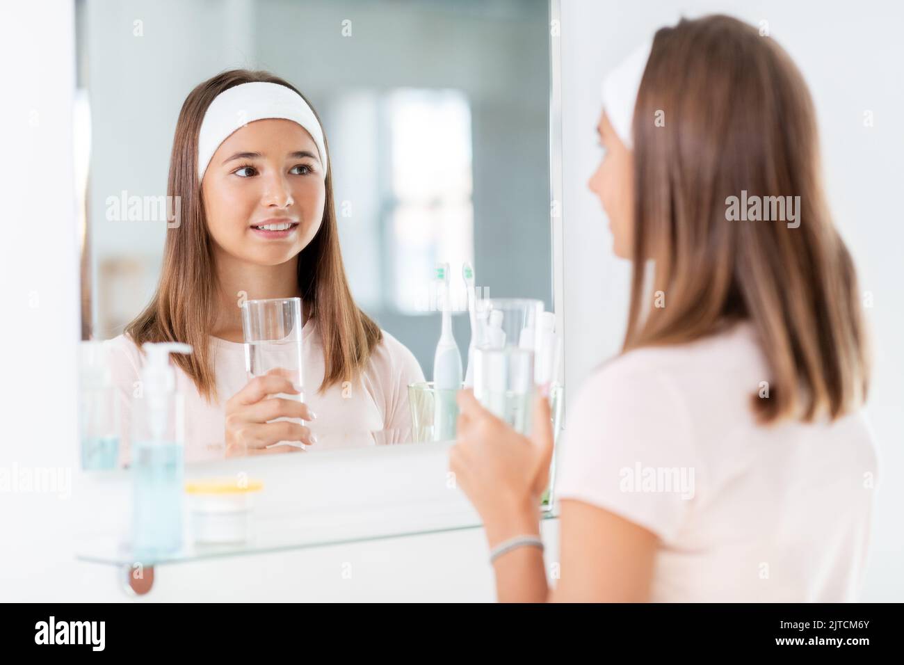 teenage girl with glass of water looking in mirror Stock Photo
