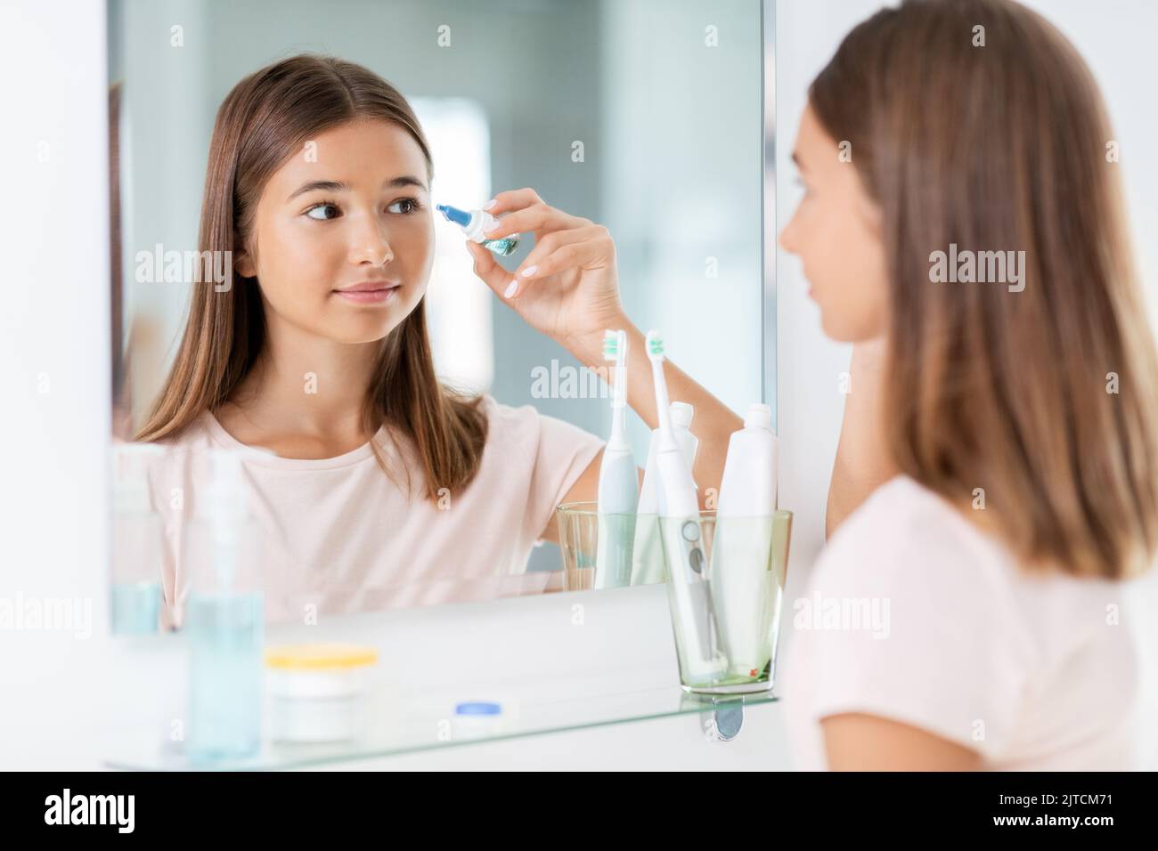 teenage girl with eye drops in front of mirror Stock Photo
