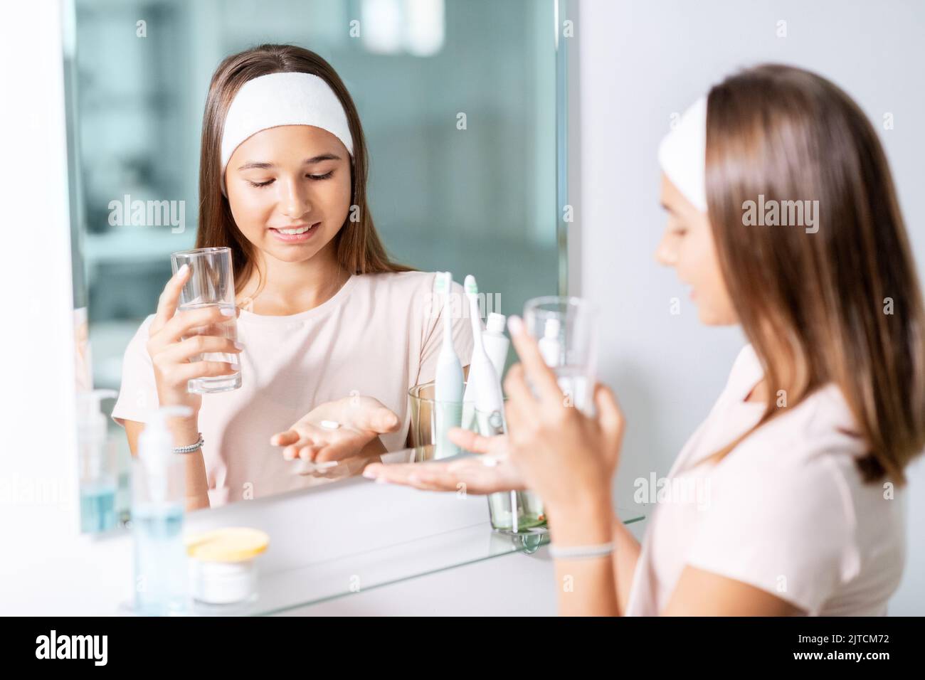 teenage girl taking pill with water at mirror Stock Photo