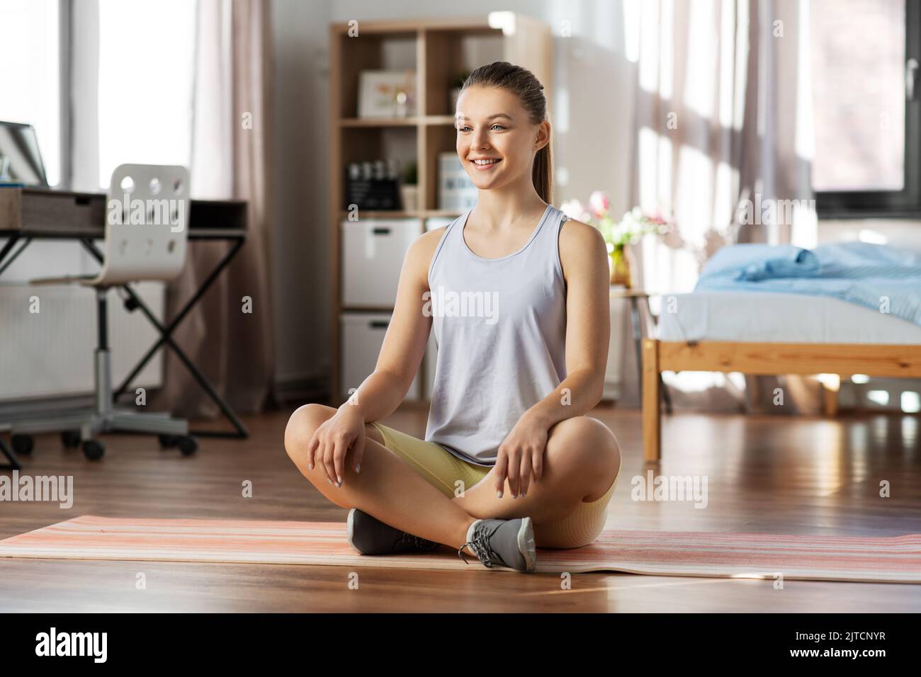 smiling teenage girl sitting on yoga mat at home Stock Photo - Alamy
