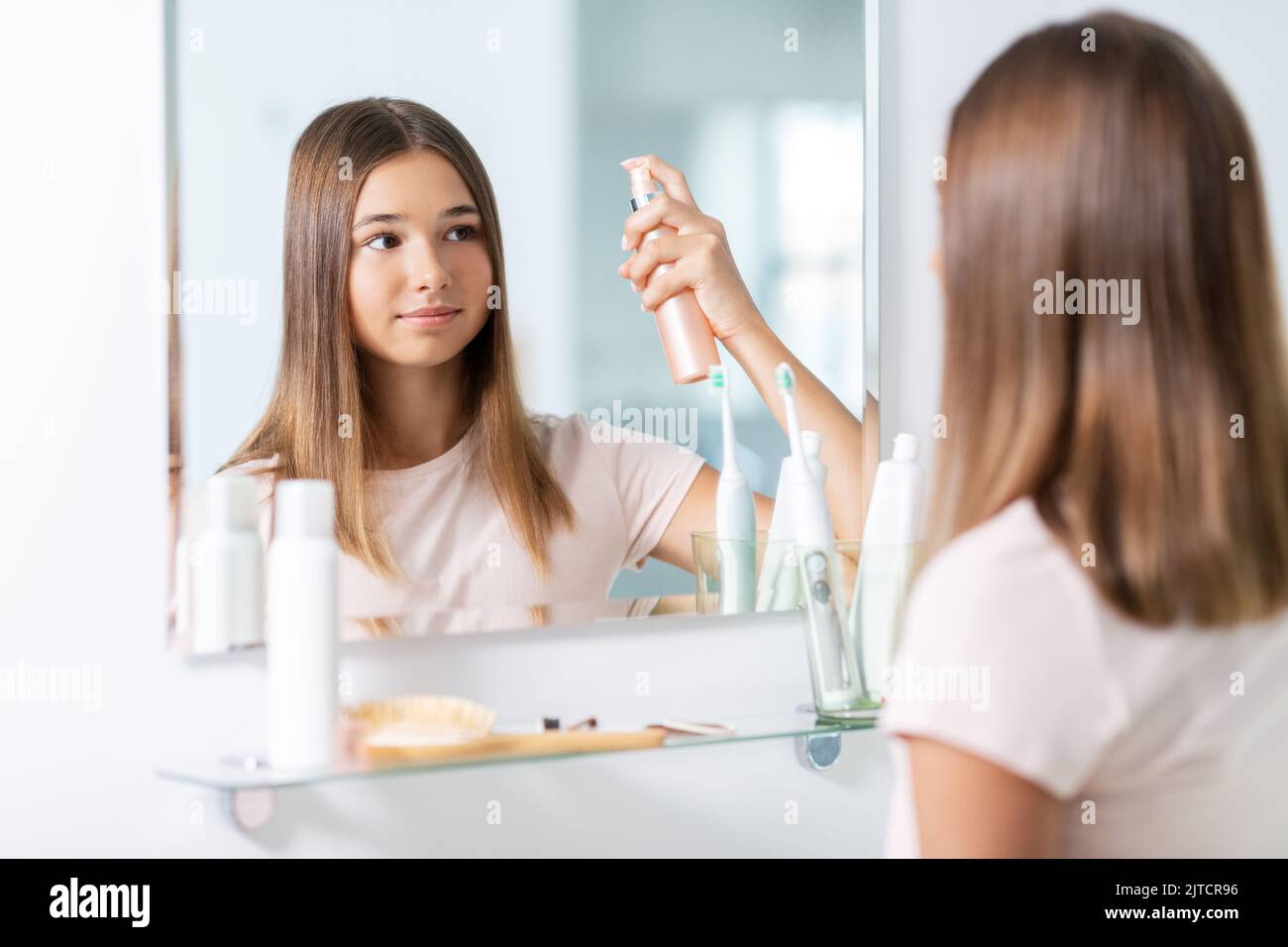 teenage girl using hair styling spray at bathroom Stock Photo