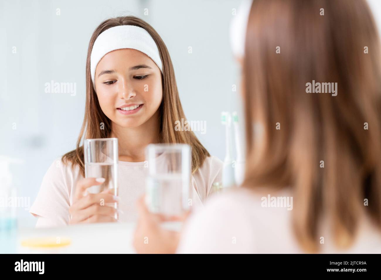 teenage girl with glass of water looking in mirror Stock Photo