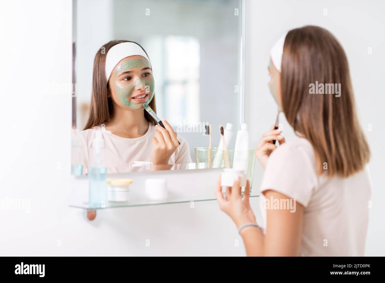 teenage girl applying mask to face at bathroom Stock Photo
