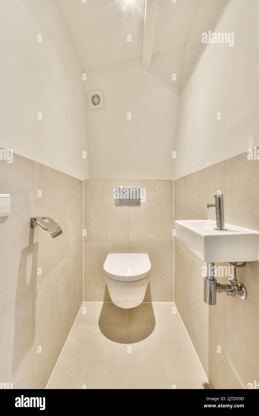 Interior of narrow restroom with sink and wall hung toilet with white