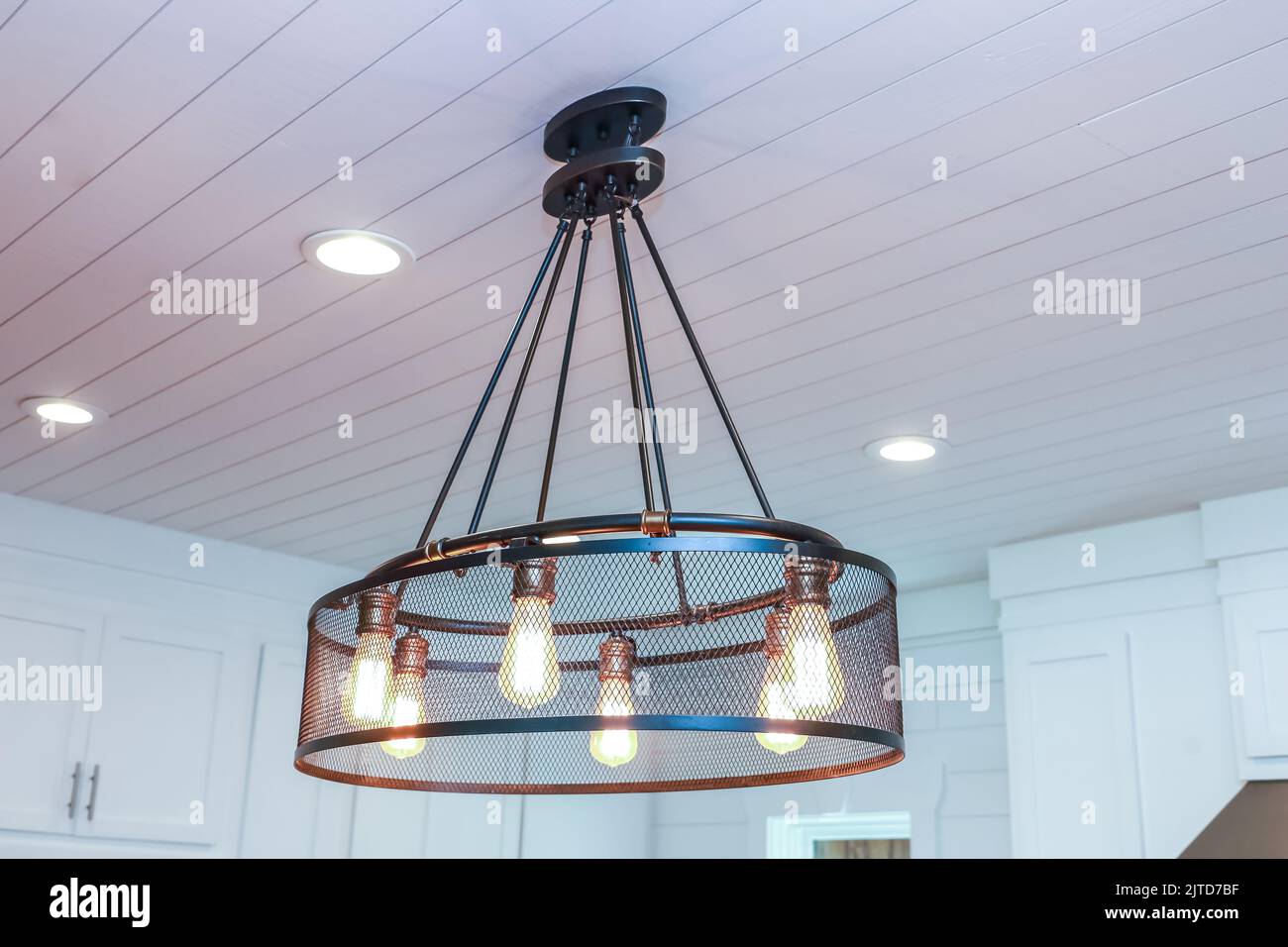 An industrial lighting fixture with Edison bulbs in an updated and remodeled all white modern kitchen Stock Photo