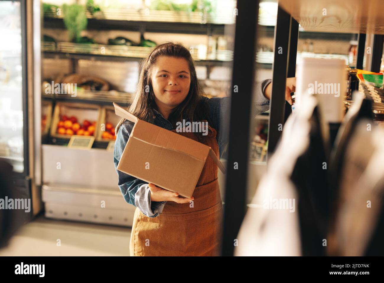 Store worker with Down syndrome restocking food products onto the shop shelves. Empowered woman with an intellectual disability working as a shopkeepe Stock Photo