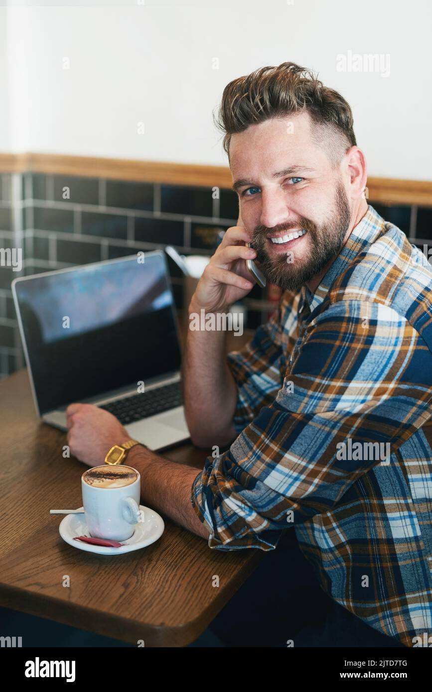 The wifi here is as good as the coffee. Portrait of a young man using his cellphone and laptop while sitting in a cafe. Stock Photo