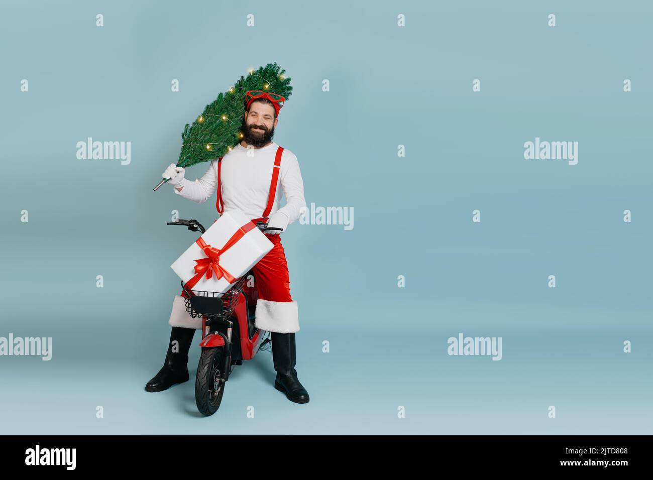 A young adult man in his 40s in a red hat, suspenders and santa pants