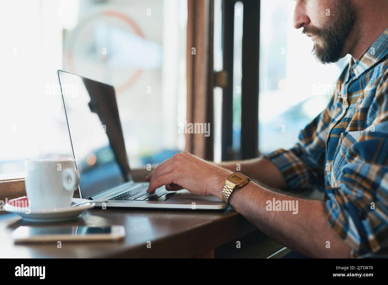 Finding inspiration in his favourite cafe. a young man using his laptop while sitting by the window in a cafe. Stock Photo