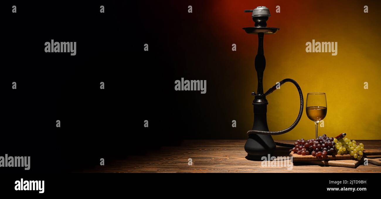 Hookah with grapes and wine on table against dark background Stock
