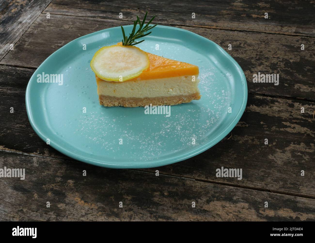 Lemon fruit slice on Cheesecake pie on blue color plate, Sweet food with brown table in background Stock Photo