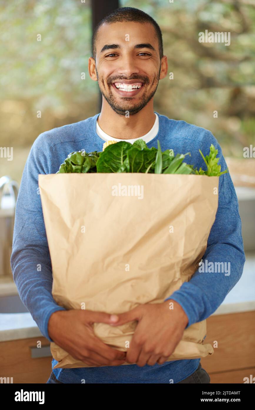Its strictly organic for me. Cropped portrait of a handsome young man standing in the kitchen with his groceries. Stock Photo