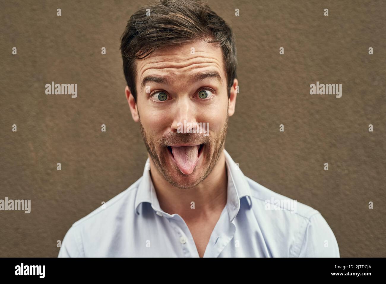 I know just how to crack you up. Portrait of a young man pulling a funny face against a dark background. Stock Photo
