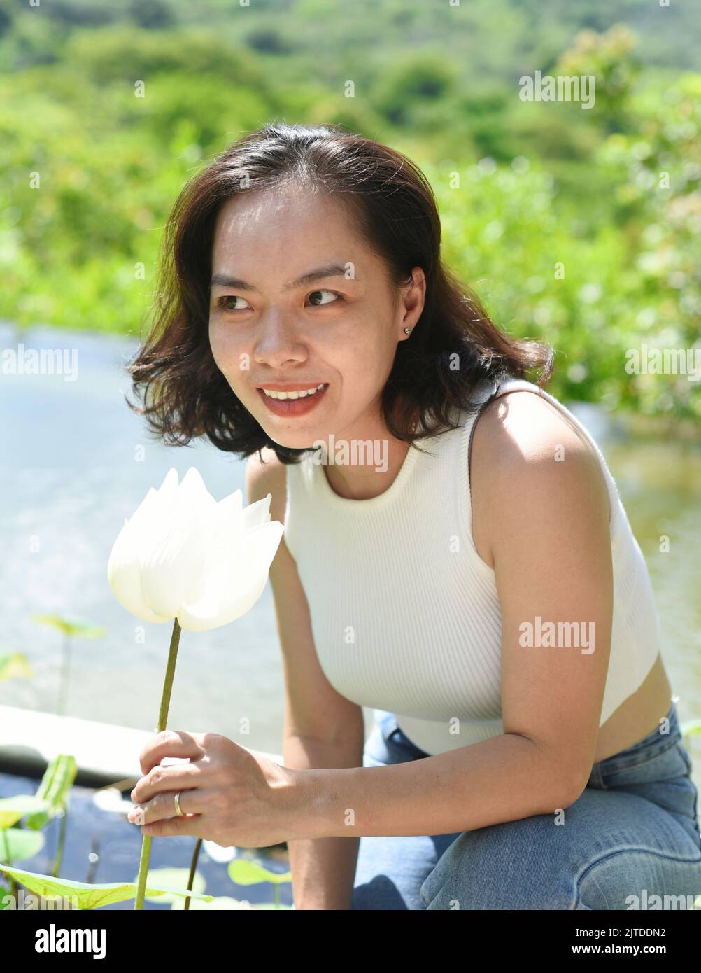 Vietnamese young woman smiling and smelling a white lotus in Vietnam Stock Photo