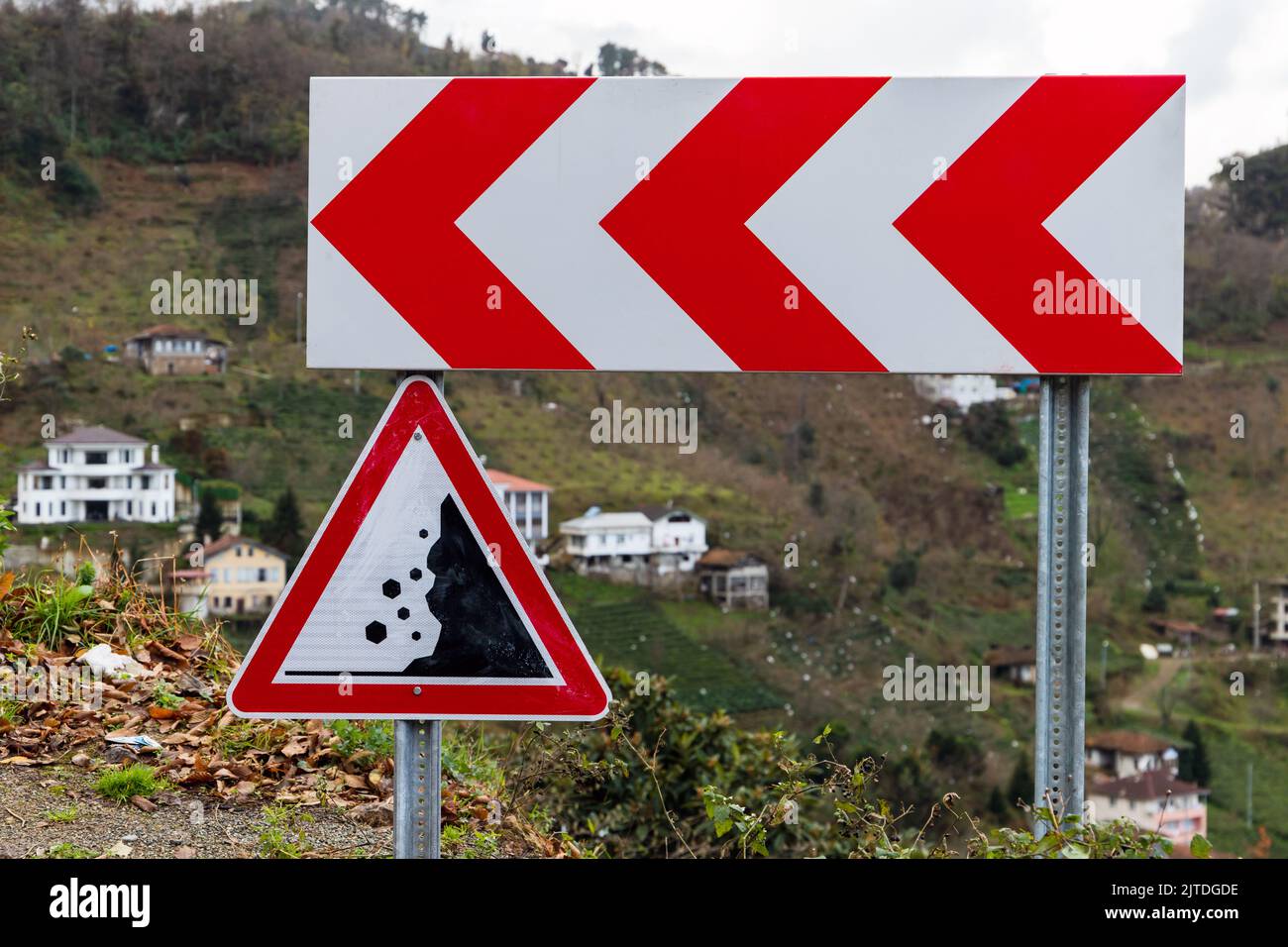 Dangerous turn and Falling rocks. Road signs mounted on a roadside of a mountain road Stock Photo