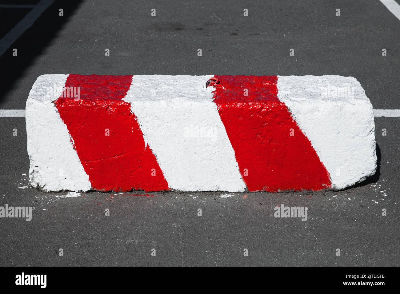 Road block made of concrete with warning red white diagonal striped pattern lays on an urban road Stock Photo