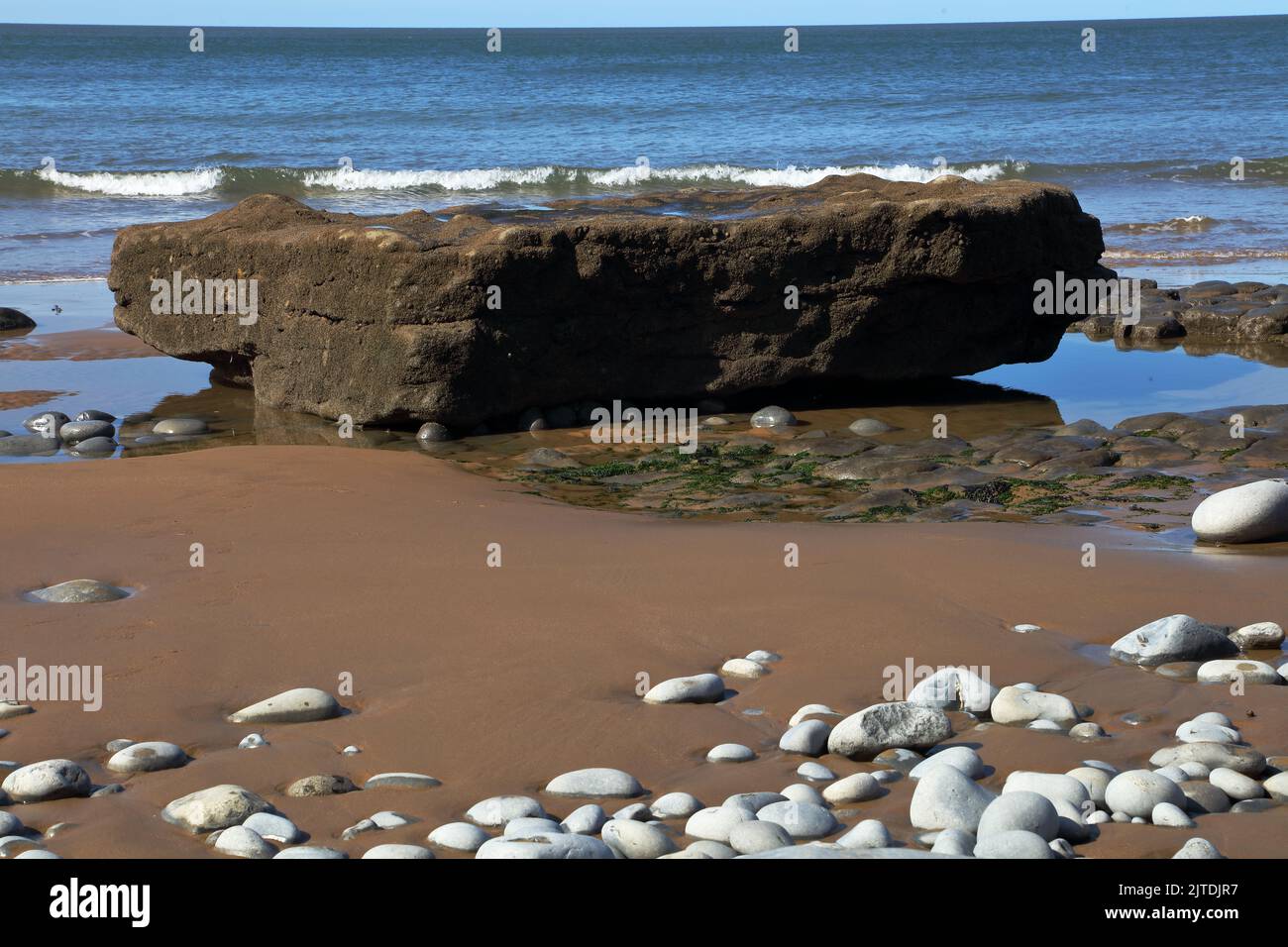 A day on the beach as the tide goes out leaving large rocks, sand and pebbles exposed ready for the Bucket and Spade set to arrive. Stock Photo