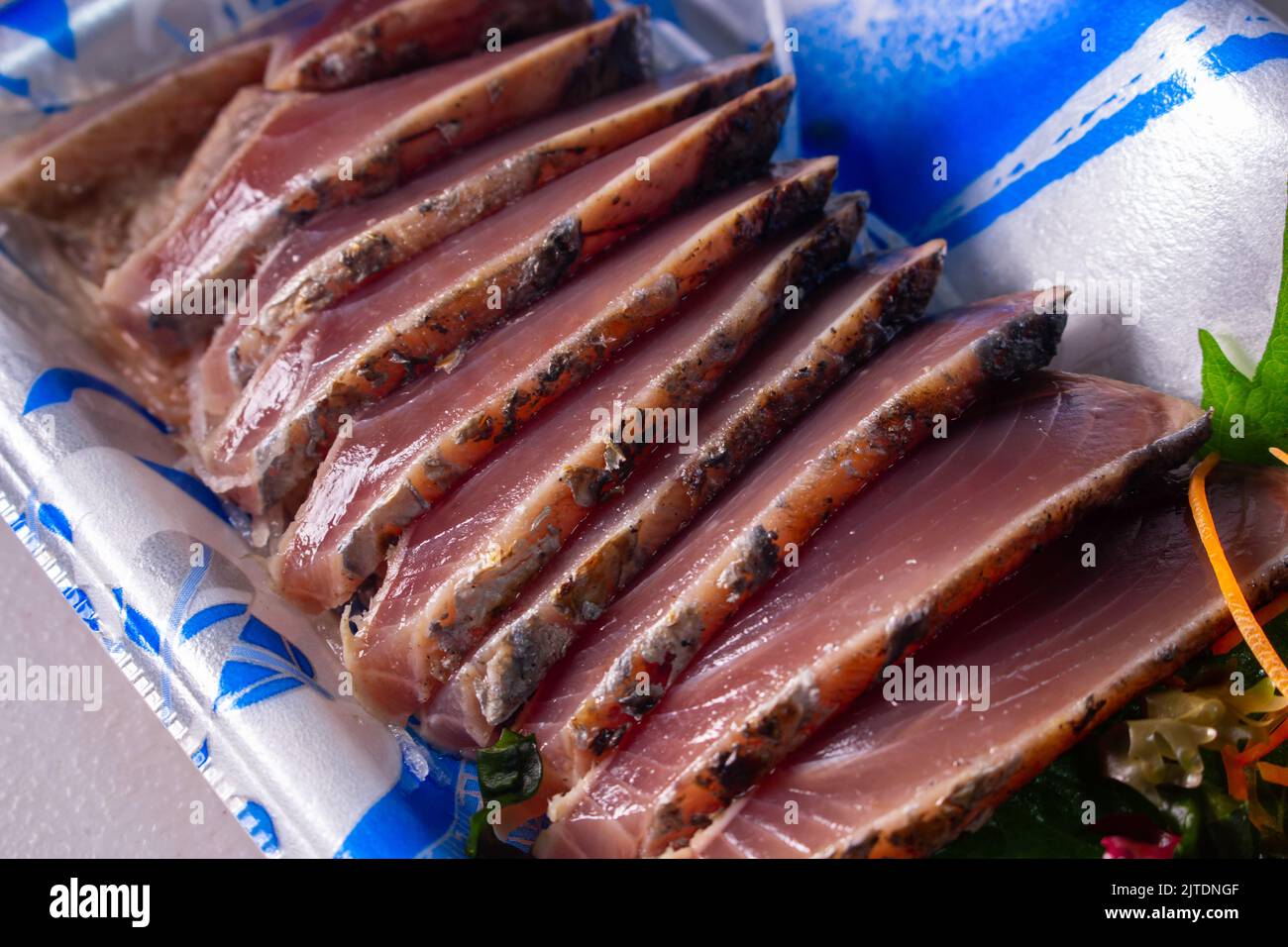 Closeup takeout Katsuo-no-Tataki (lightly broiled, sliced bonito sashimi) in supermarket food container. Stock Photo