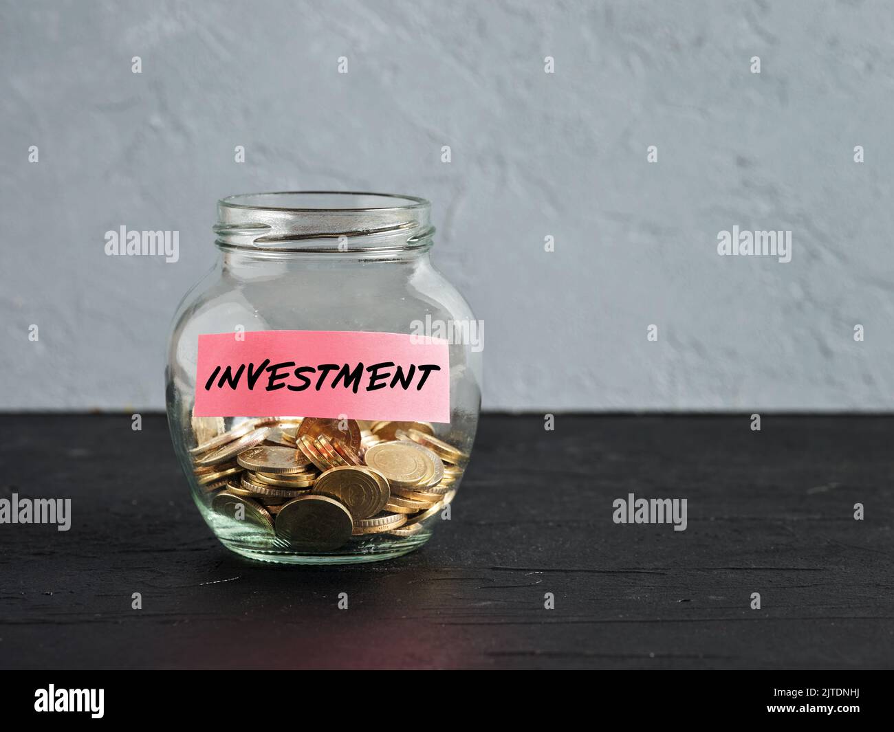 Glass jar with coins and the word investment on a label. Investing in a new business project or real estate. Saving money. Capital accumulation, distr Stock Photo